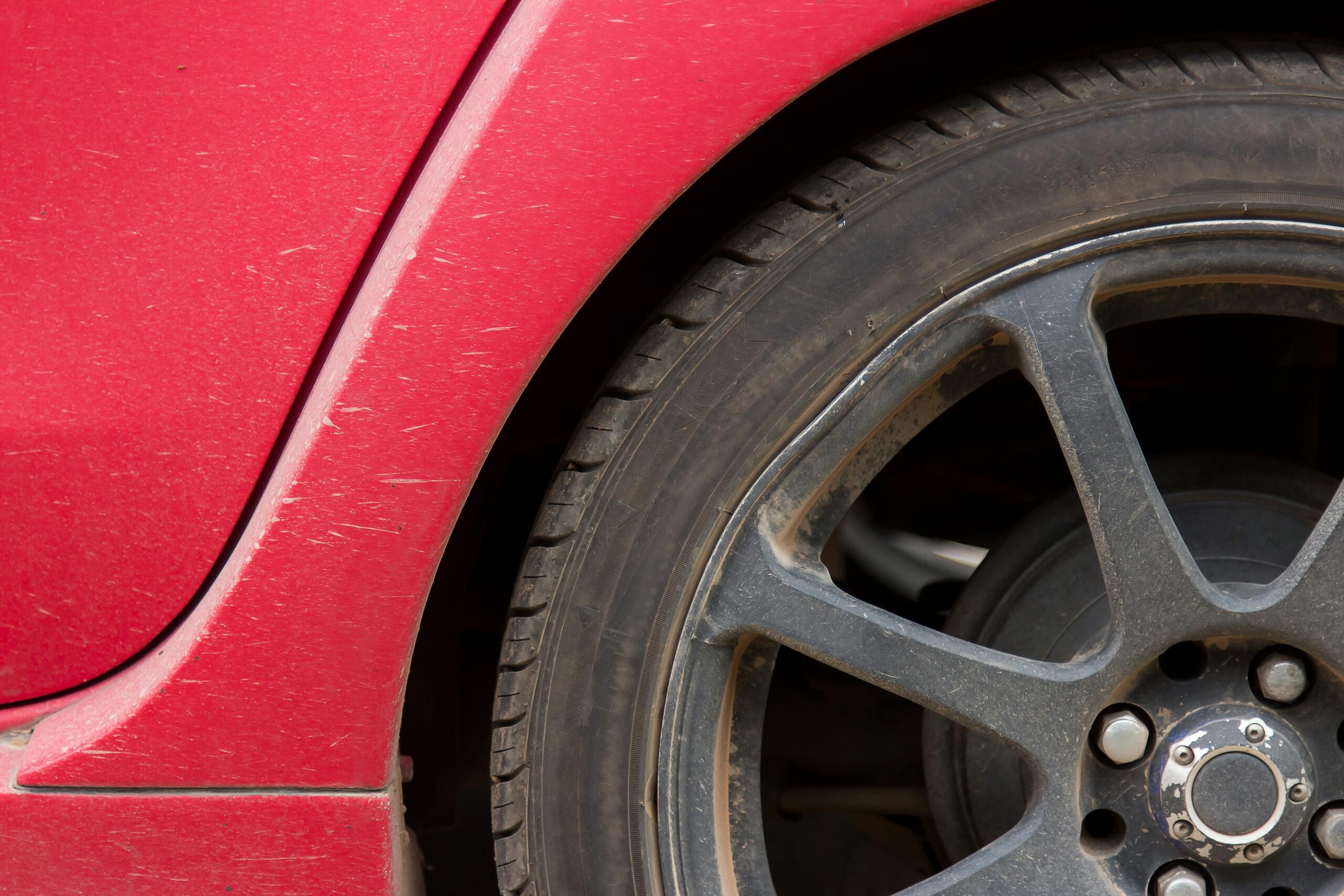 dirty red car with scratches and dirty wheels